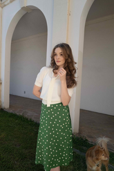 a lady in a white bow tie neck shirt and a green skirt with polka dots